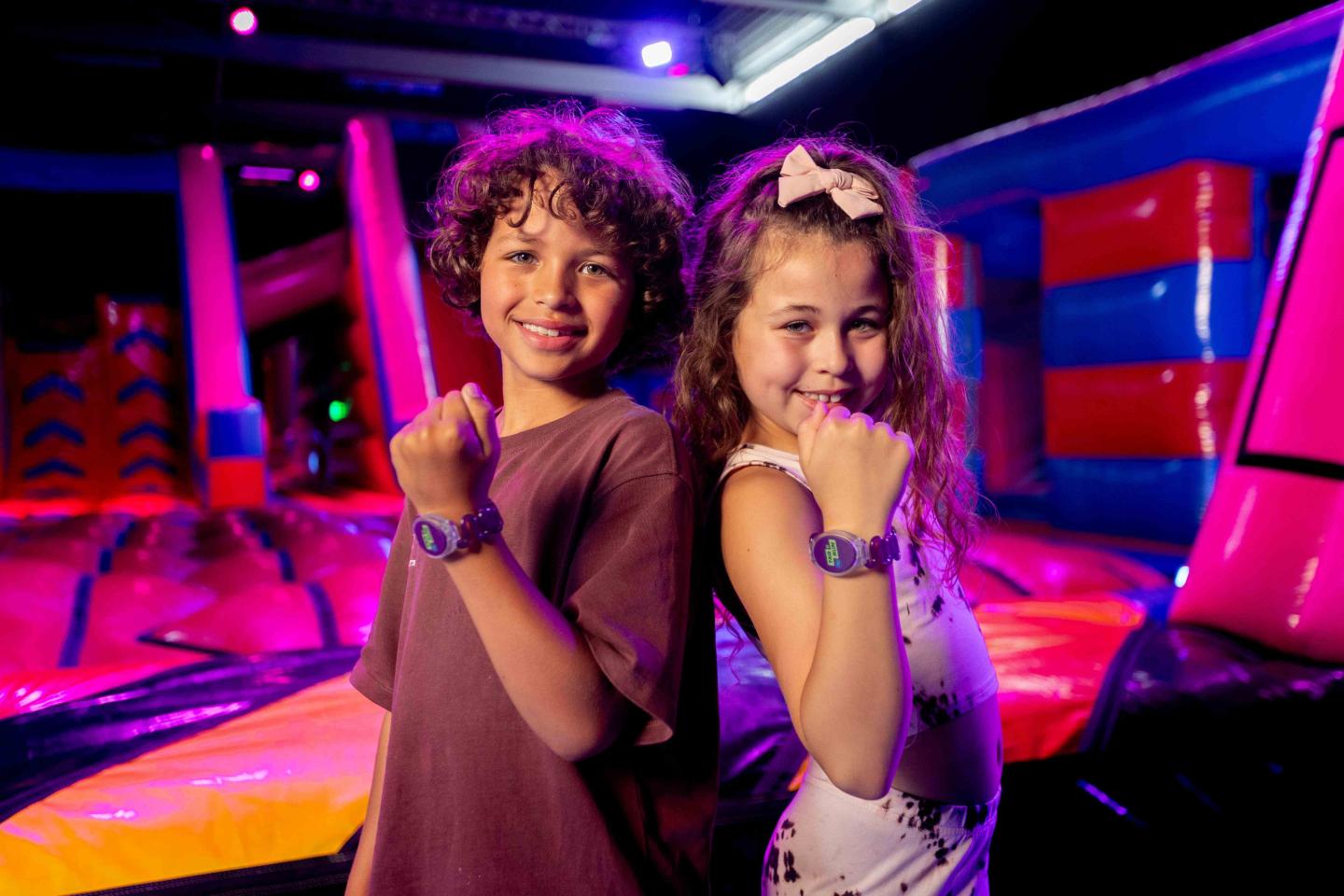 wee kinderen poseren trots met hun JB Tag & Run polsbandjes in een opblaasbare speelomgeving