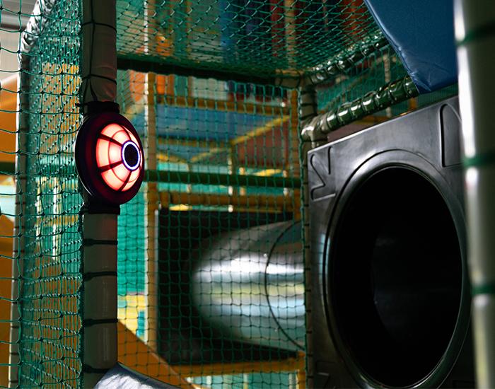 Interactieve JB-TAG speellamp in een indoor speelparadijs, gemonteerd in een klimstructuur naast een glijbaan, klaar om getagd te worden voor punten