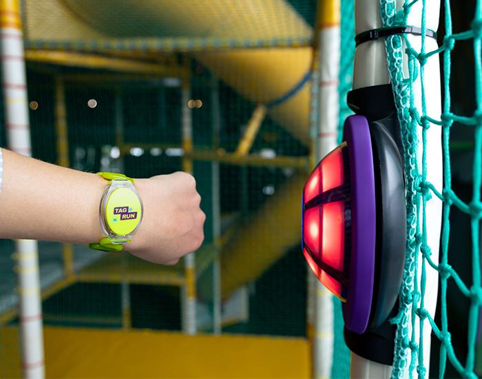 Kind draagt TAG & RUN speelbandje en activeert een rode JB-TAG sensor in een indoor speelparadijs.