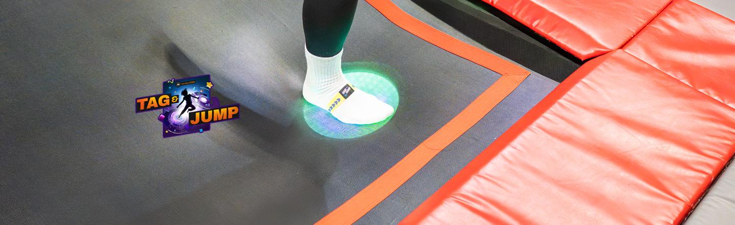 Voet met sensorbandje activeert groene lichtspot op trampoline tijdens Tag & Jump spel.
