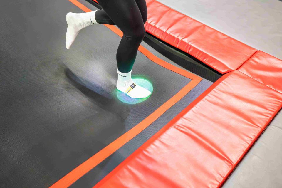 Voet met sensorbandje activeert groene lichtspot op trampoline tijdens Tag & Jump spel.